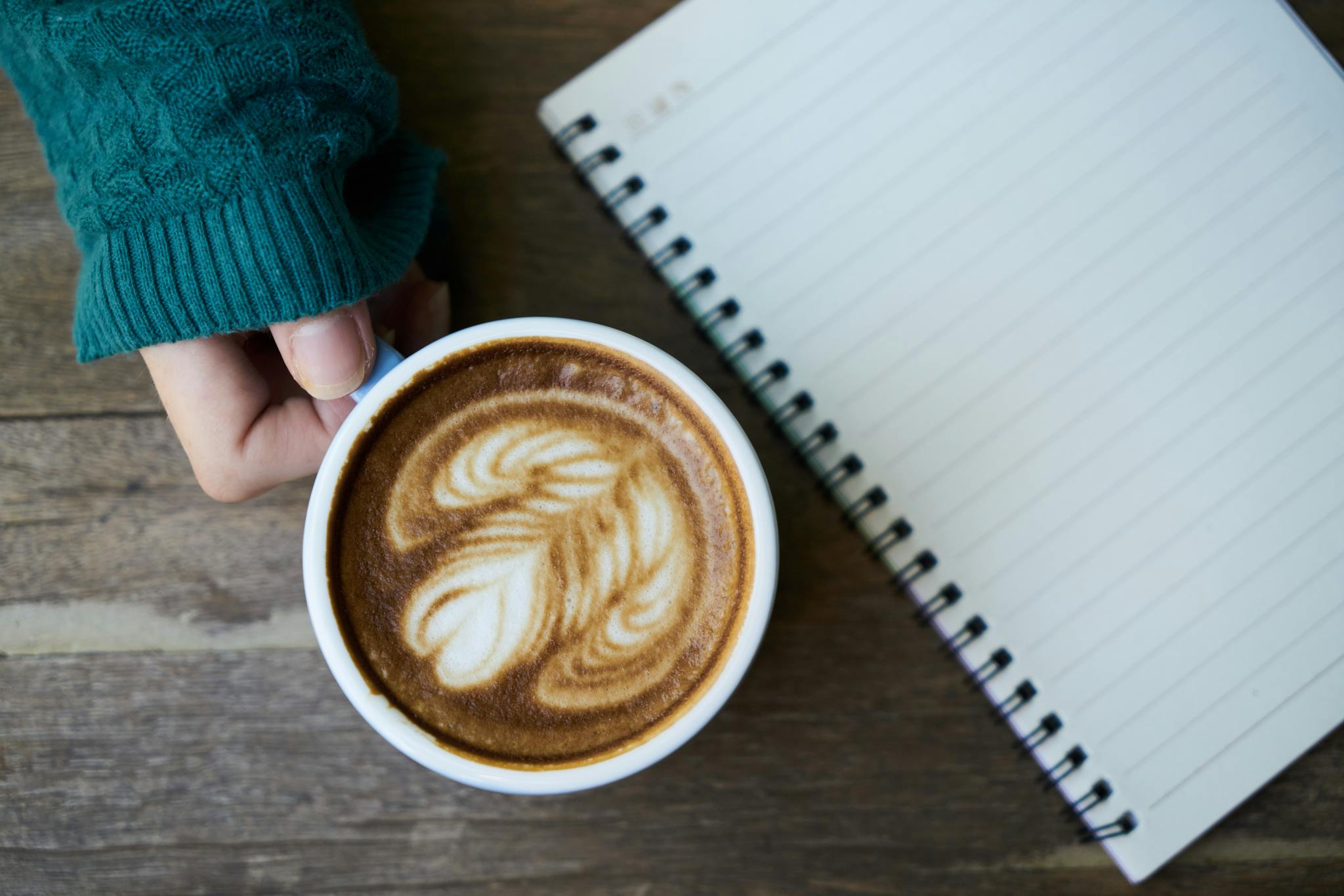 Person Holding White Ceramic Mug Beside Notebook